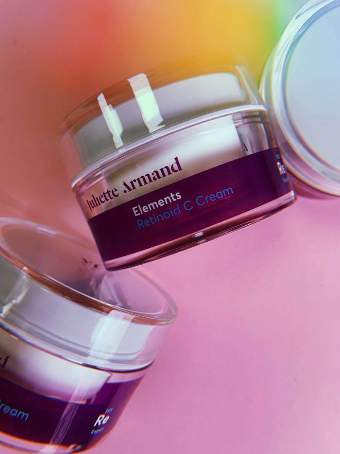 Elegant display of cosmetic jars containing retinoid C cream against a pink backdrop.