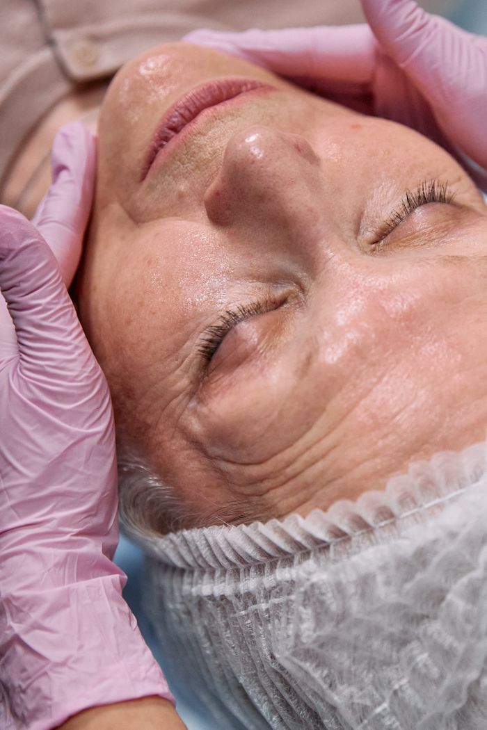 about-us-02 Close-up of an elderly woman with eyes closed receiving a relaxing spa facial treatment.